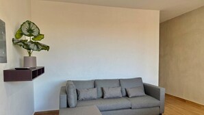 Ein graues Ecksofa mit passendem Hocker in einem modernen Wohnzimmer mit Holzboden und minimalistischem Design.