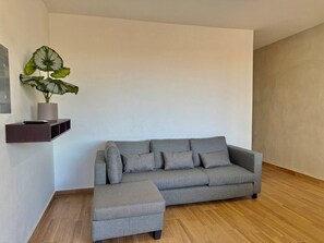 Ein graues Ecksofa mit passendem Hocker in einem modernen Wohnzimmer mit Holzboden und minimalistischem Design.