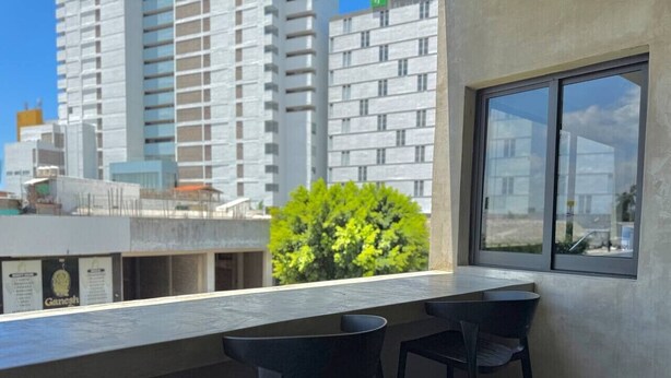 Ein Balkon mit zwei Stühlen, einem Fenster und Blick auf ein Gebäude mit einem grünen Baum im Hintergrund.