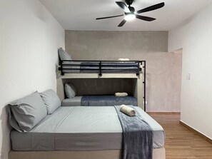 Ein Zimmer mit Etagenbett, Einzelbett, Deckenventilator und Holzboden.