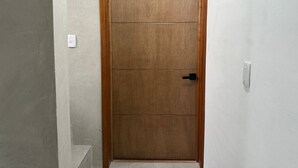 Eine geschlossene Holztür mit schwarzem Griff, weißen Wänden und einem Lichtschalter an der Wand.