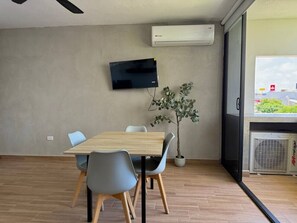 Ein moderner Besprechungsraum mit einem Holztisch, grauen Stühlen, einer Topfpflanze und einem wandmontierten Flachbildfernseher.