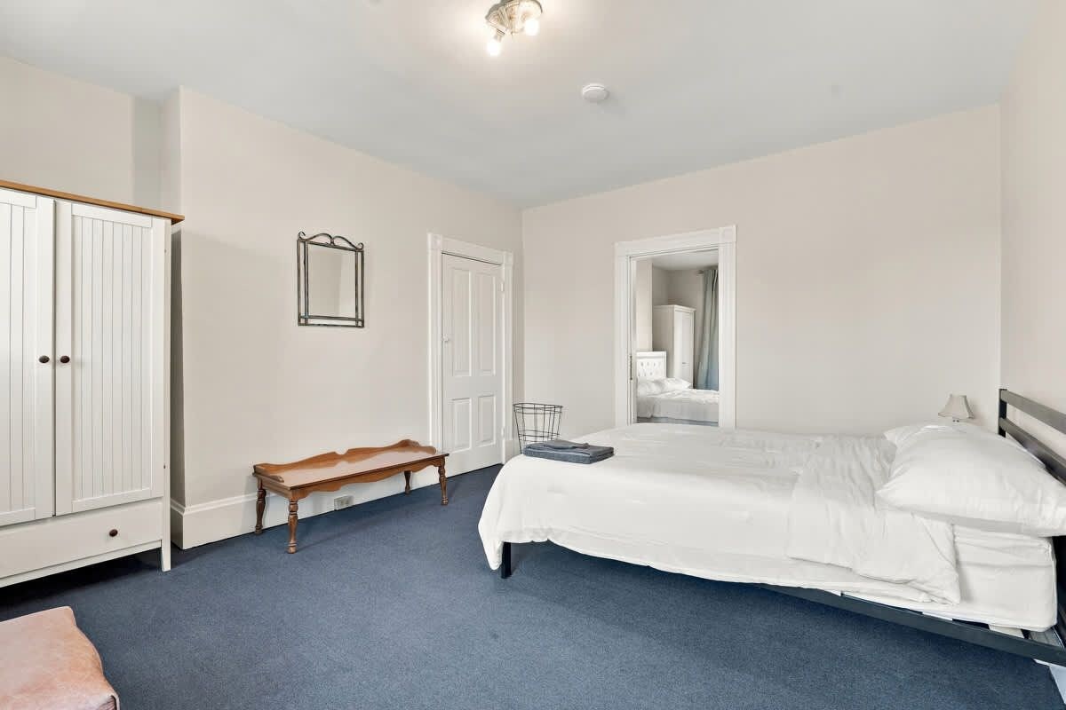 A bedroom with a large bed, a wardrobe, a bench, and a mirror.