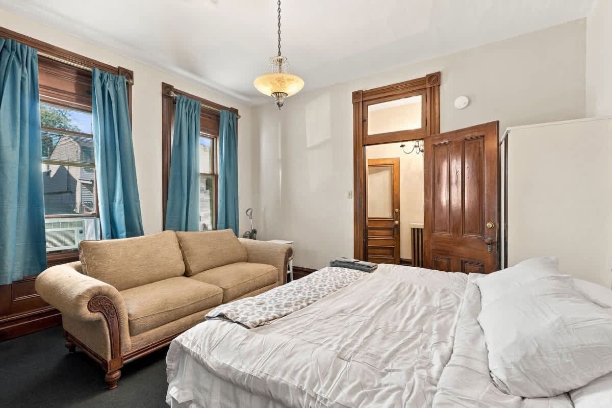 A bedroom with a bed, a sofa, a dresser, and a window with curtains.