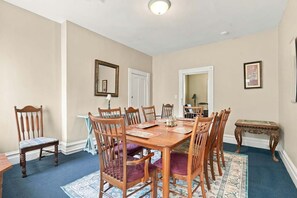 A dining room with a wooden table and chairs, a blue carpet, and a small side table. - Walk to E Carson St · 4BR Sleeps 10 · South Side (Pittsburgh)