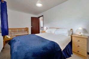 Une chambre à coucher comprenant un lit, une table de chevet, une commode, un berceau et une porte.