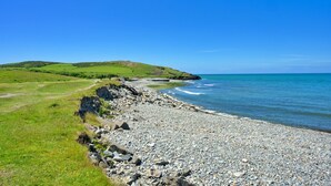 Un paisaje costero con playa de guijarros, campos verdes y cielo azul despejado.