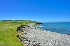 A coastal landscape with a pebbly beach, grassy fields, and a clear blue sky. - Charming Dorset Coach House for 6 (Caernarfon)