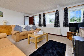 A furnished living room with a sofa, a coffee table, a television, and a window with curtains. - Charming Dorset Coach House for 6 (Caernarfon)