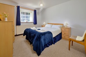 A bedroom with a bed, bedside tables, a chair, a window with curtains, a radiator, and a lamp. - Charming Dorset Coach House for 6 (Caernarfon)