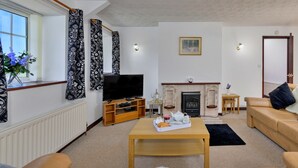 Una sala de estar con sofá, una mesa de centro, televisor, chimenea y una ventana con cortinas.