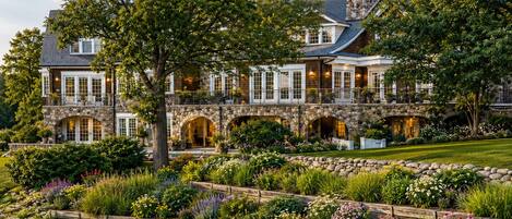 A large stone house with multiple balconies and a well-maintained garden with a pond.