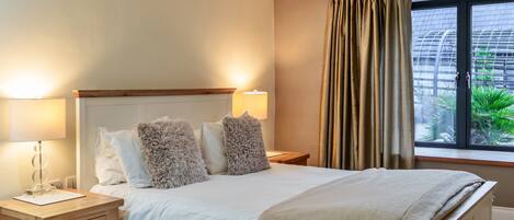 A neatly made bed with fluffy pillows, a bedside table with a lamp, and a window with curtains.