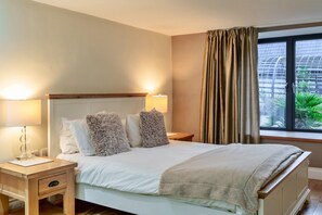 Ein ordentlich bezogenes Bett mit flauschigen Kissen, ein Nachttisch mit Lampe und ein Fenster mit Vorhängen.