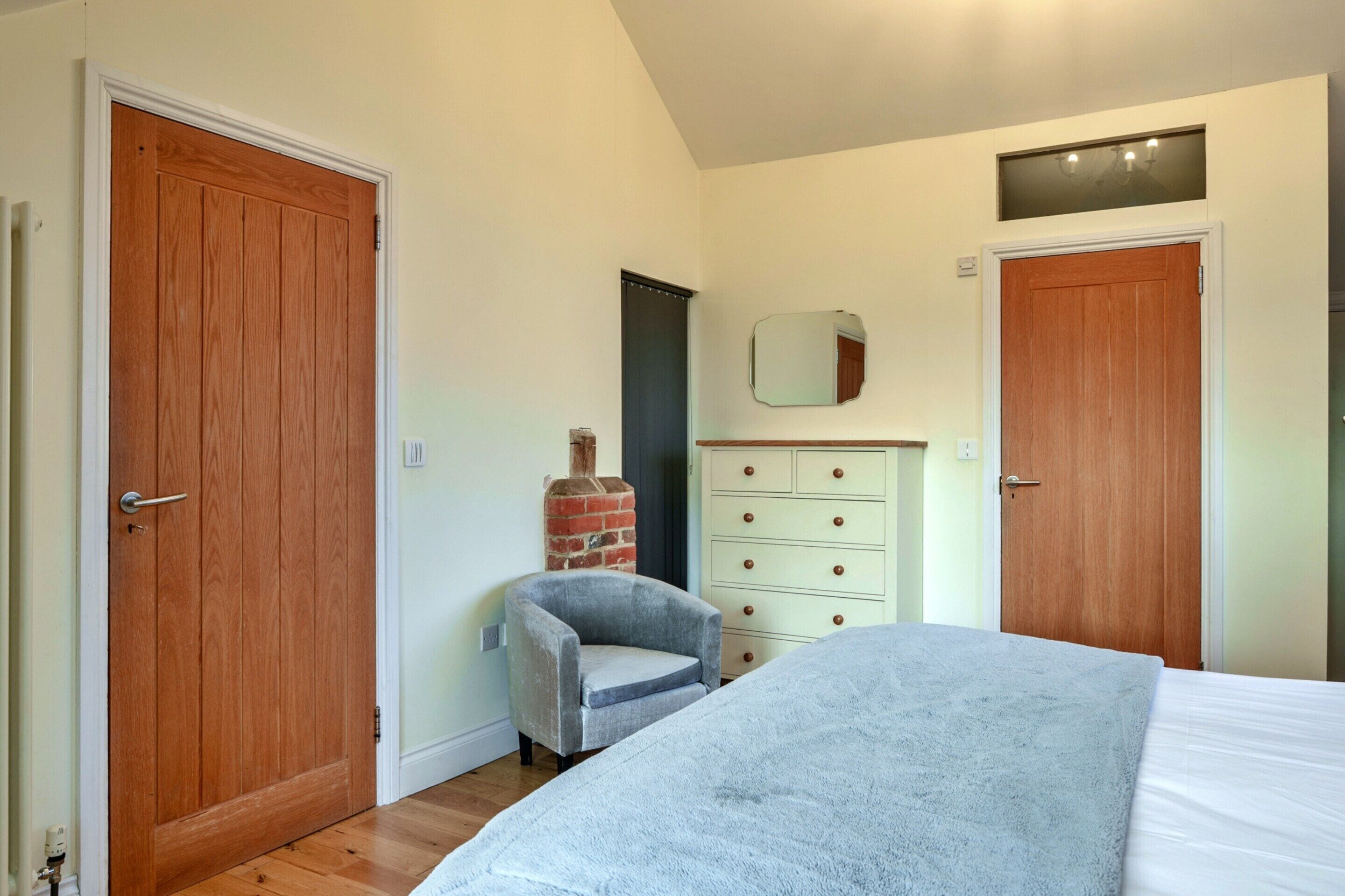 A bedroom with a bed, a dresser, a chair, and two doors.