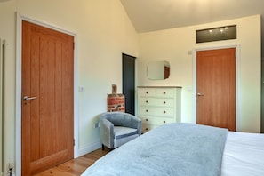 A bedroom with a bed, a dresser, a chair, and two doors. - Stylish Barn Retreat for 8 (Wimborne)