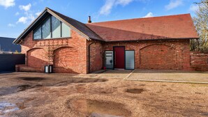 A single-story brick building with a red-tiled roof, a large window on the left, and a door with a red frame. - Stylish Barn Retreat for 8 (Wimborne)