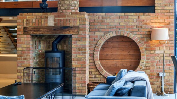 A cozy living area with a brick fireplace, a round wooden feature, and a modern sofa. - Stylish Barn Retreat for 8 (Wimborne)