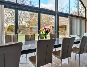 Ein Essbereich mit Tisch und Stühlen, einer Blumenvase und Blick auf einen Garten durch große Fenster.
