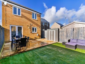 A residential backyard with a patio, a dining table with chairs, a covered seating area, and a wooden fence. - House Near Golf Course Llanelli (Llanelli)