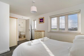 A hotel room with a bed, a window with blinds, a radiator, a door leading to a bathroom, and a picture on the wall. - House Near Golf Course Llanelli (Llanelli)