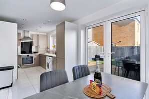 A modern kitchen with a built-in oven, a washing machine, and a dining area with a table and chairs. - House Near Golf Course Llanelli (Llanelli)