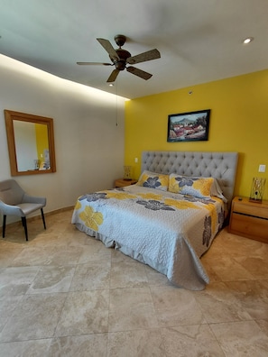 A bedroom with a bed, a chair, a ceiling fan, a wall-mounted picture, and a nightstand. - Beautiful 2 BR in El Dorado with gorgeous views! (Jal.)