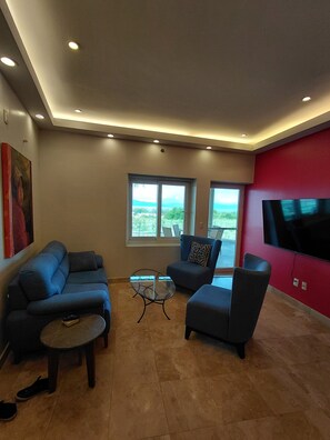 A living room with a sofa, armchair, and coffee table, a TV mounted on a red wall, and a window with a view. - Beautiful 2 BR in El Dorado with gorgeous views! (Jal.)