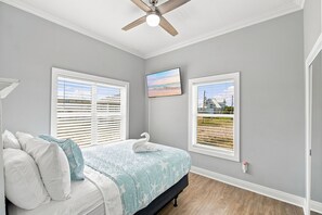 A bedroom with a bed, two windows with blinds, a ceiling fan, and a wall-mounted TV. - Barefoot Treasure Gulf Views, Canal Front & Pool (Navarre)