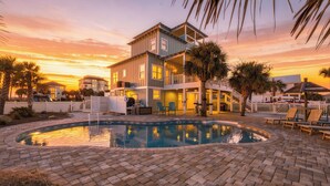 A two-story house with a swimming pool, surrounded by palm trees and a sunset sky. - Barefoot Treasure  Gulf Views, Canal Front & Pool (Navarre)