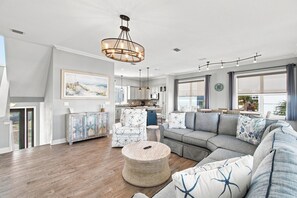 A spacious living room with a large sectional sofa, a round ottoman, and a dining area in the background. - Barefoot Treasure Gulf Views, Canal Front & Pool (Navarre)