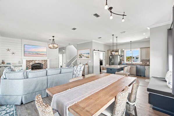 A spacious living area with a fireplace, a dining table, and a kitchen with a view. - Barefoot Treasure Gulf Views, Canal Front & Pool (Navarre)