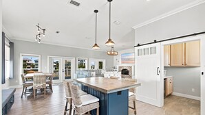 A spacious kitchen with a central island, a dining area with wicker furniture, and a view of the outside through large windows. - Barefoot Treasure  Gulf Views, Canal Front & Pool (Navarre)