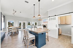 A spacious kitchen with a central island, a dining area with wicker furniture, and a view of the outside through large windows. - Barefoot Treasure  Gulf Views, Canal Front & Pool (Navarre)
