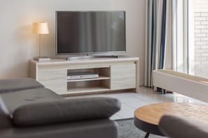 Ein modernes Wohnzimmer mit einem Flachbildfernseher auf einem Holzschrank, einem Sofa, einem Couchtisch und einer Heizung.