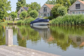 A houseboat docked at a calm water body with a wooden dock in the foreground. - Waterfront Bungalow With Garden (Makkum)