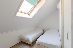 A small, single-room with a sloped ceiling and a skylight. There are two single beds with white bedding. - Waterfront Bungalow With Garden (Makkum)