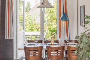 Une table à manger avec des chaises, une bouteille de vin et un luminaire suspendu bleu.