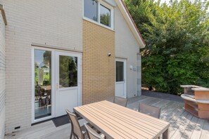 Ein zweistöckiges Haus mit einer Terrasse, auf der ein Holztisch und Stühle stehen.