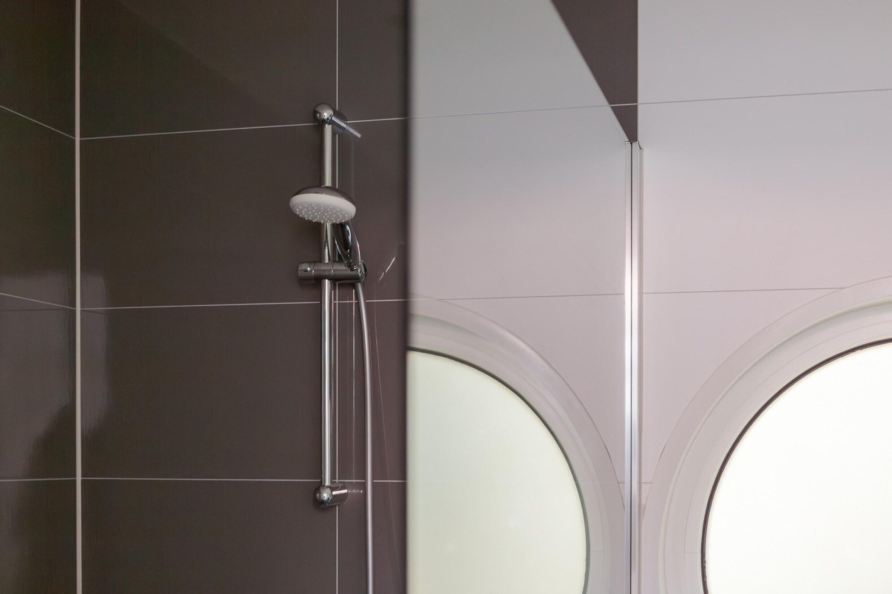 A shower with a handheld showerhead and a handheld scrubber.