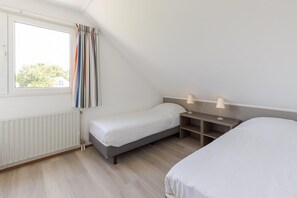 Une chambre avec un lit simple, une table de chevet avec une lampe, une fenêtre avec des rideaux et un radiateur.