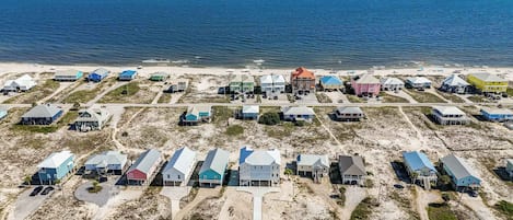 A coastal residential area with houses on stilts, a beach in the background, and a clear view of the ocean.