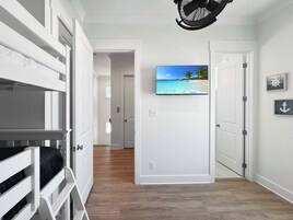 Una habitación con literas, un televisor montado en la pared y una puerta que da a otra habitación.