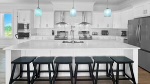 A modern kitchen with white cabinetry, stainless steel appliances, and a central island with bar stools.