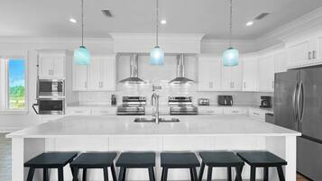 Uma cozinha moderna com armários brancos, eletrodomésticos de aço inoxidável e uma ilha central com banquetas.