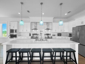 Una cocina moderna con armarios blancos, electrodomésticos de acero inoxidable y una isla central con taburetes de bar.