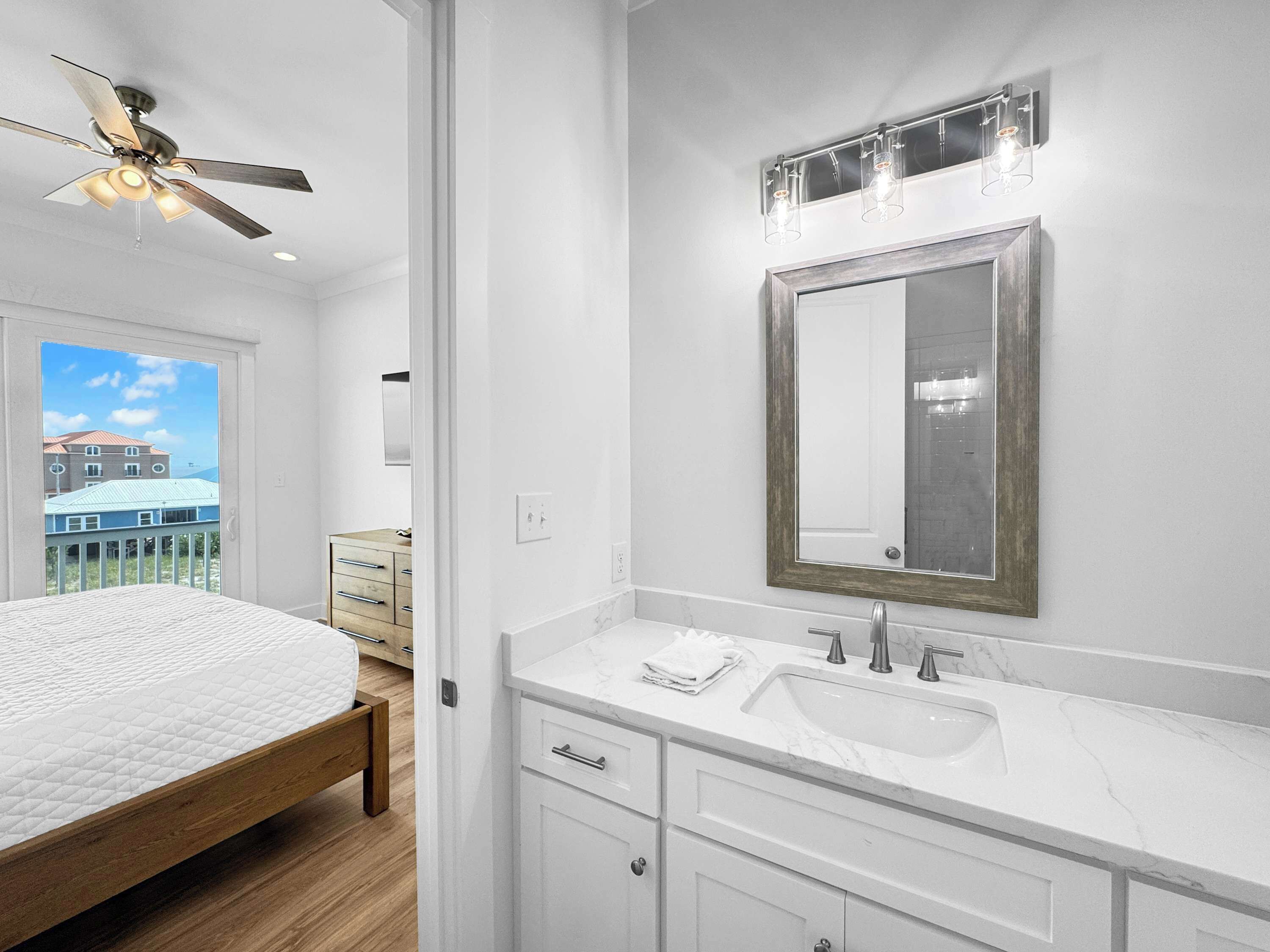 Un baño moderno con un espejo grande, tocador blanco y ventilador de techo.
