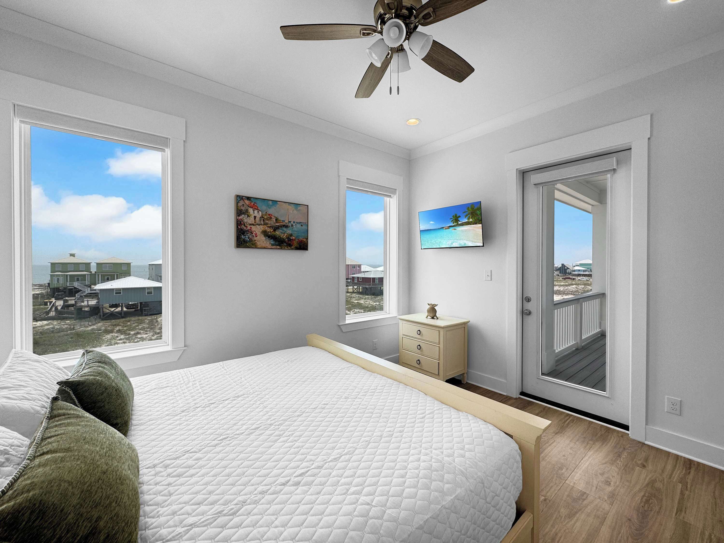 A bedroom with a bed, a dresser, a television, and a door leading to a balcony.