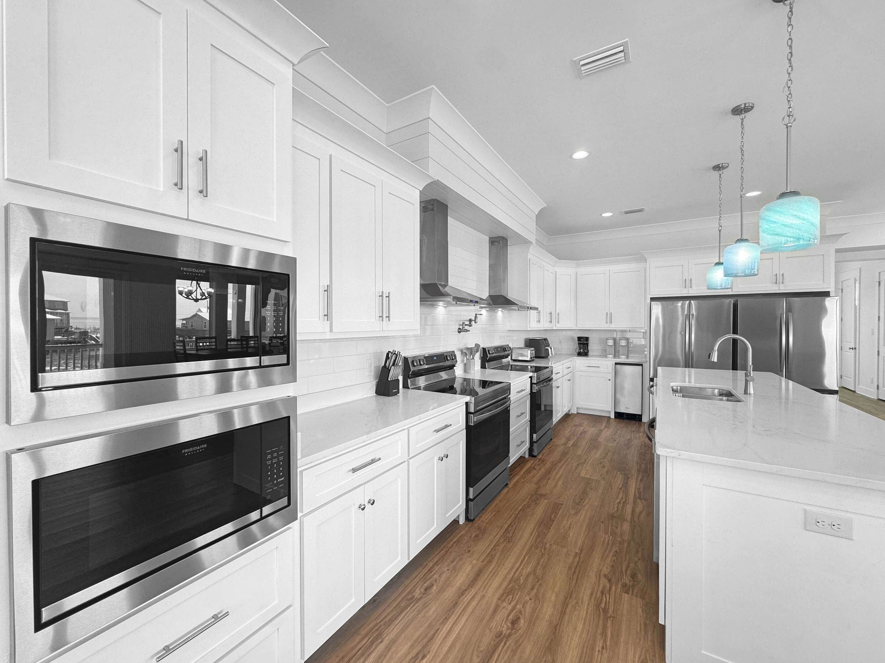 A modern kitchen with stainless steel appliances, white cabinetry, and a wooden floor.