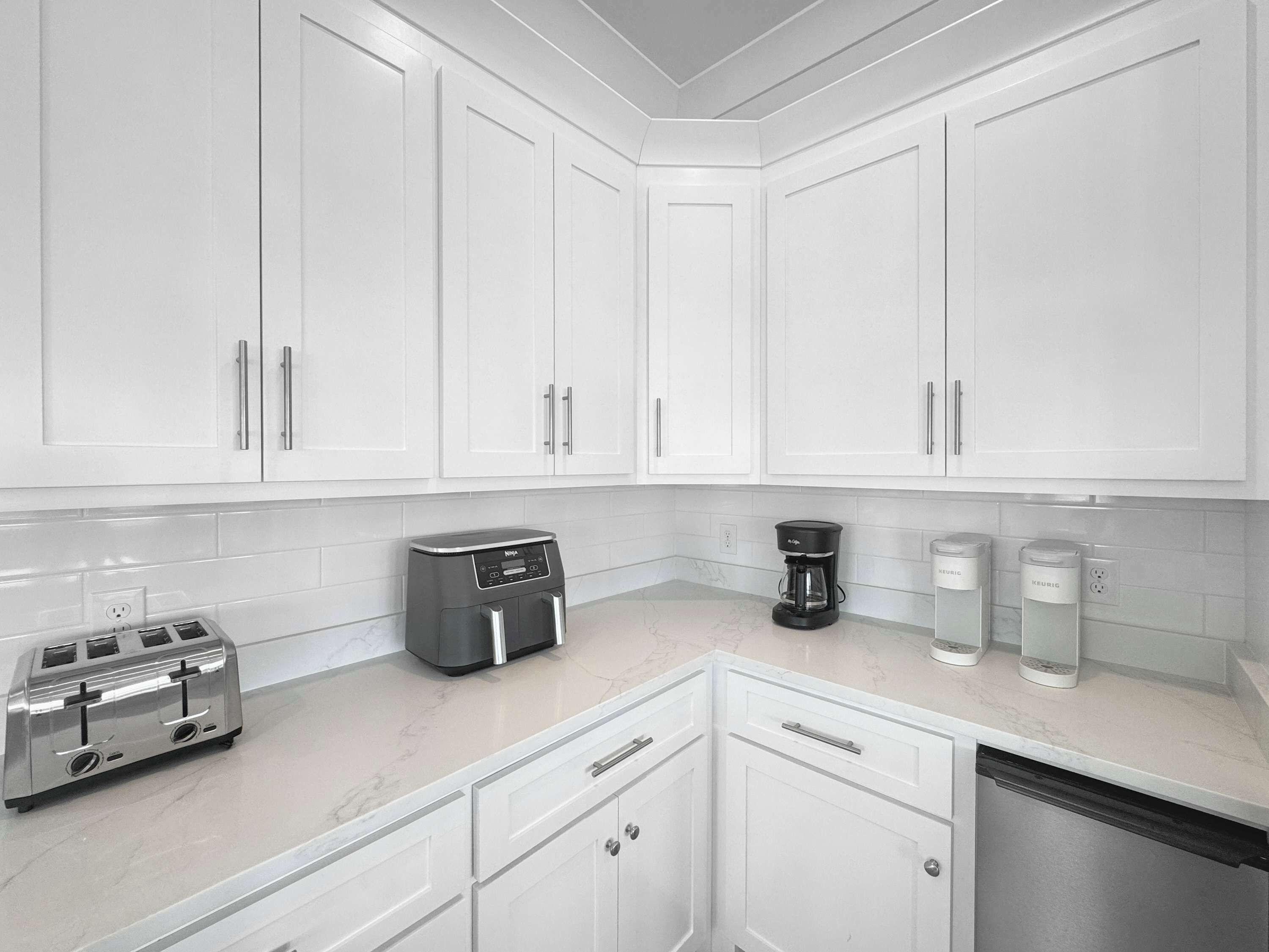 A modern kitchen with white cabinetry, a toaster, a coffee maker, and two coffee dispensers.